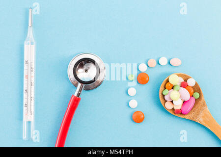 Termometro lo stetoscopio e il cucchiaio di legno con le pillole come modello medico o pattern su fondo azzurro Foto Stock