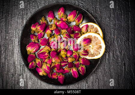 Rosa tea le gemme e le fette di limone sulla piastra scuro Foto Stock