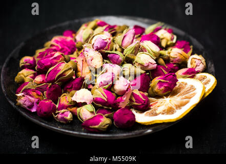 Rosa tea le gemme e le fette di limone sulla piastra scuro Foto Stock