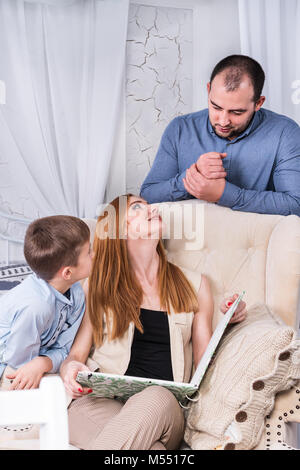 Famiglia di tre persone che studiano un libro seduto in una sedia Foto Stock