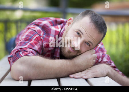 Barbuto uomo bello giacente su un banco di lavoro Foto Stock