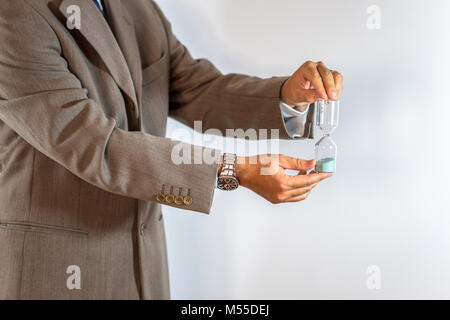 Imprenditore tenendo una clessidra isolati su sfondo bianco - Il tempo è denaro concetto. Foto Stock