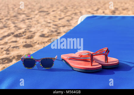 Pantofole e gli occhiali da sole sul lettino in spiaggia Foto Stock