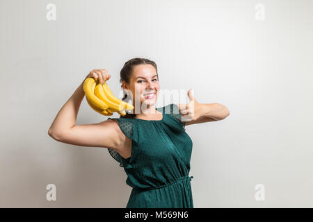 Affascinante brunette in abito verde mostra Pollice su per il cibo sano Foto Stock