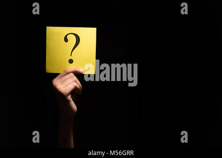 Mano che tiene un foglio giallo con punto interrogativo in uno sfondo scuro Foto Stock