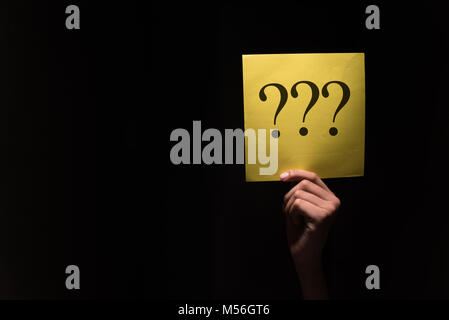 Mano che tiene un foglio giallo con punto interrogativo in uno sfondo scuro Foto Stock