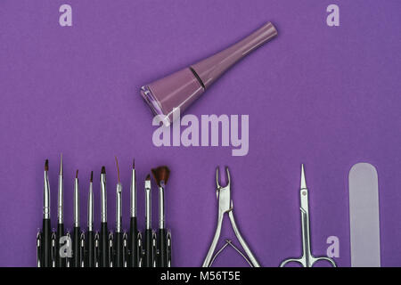 Vista dall'alto di smalto per unghie manicure e strumenti isolati su viola Foto Stock