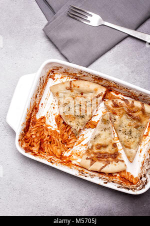 Piatto di avanzi di pasta di formaggio e aglio pane con una forchetta e tovagliolo su un grigio sfondo rustico Foto Stock