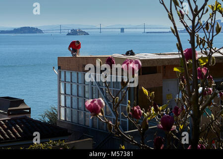 Carpenter lavora ad alta sul tetto di una casa sulla collina di Sausalito, la baia di San Francisco e Alcatraz in background. Foto Stock