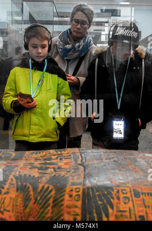 Madre e due figli (l'ascolto di audio guida attraverso le cuffie), guardando attraverso il vetro in corrispondenza di una mummia caso presso il British Museum di Londra, Inghilterra, Regno Unito. Foto Stock