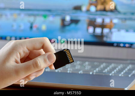 Una giovane donna di mano che tiene un nero della scheda SD con un computer portatile su uno sfondo sfocato Foto Stock