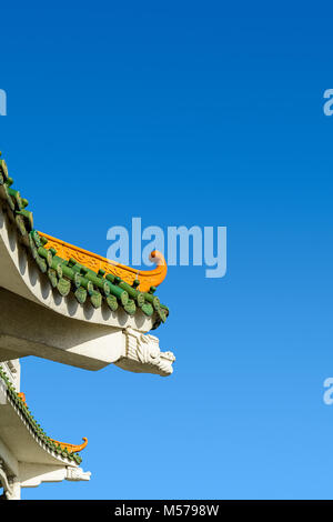 Cinese-ispirato curvo sul tetto di un edificio di stile contemporaneo con vetrate decorative tegole del tetto e a forma di drago trave di calcestruzzo contro un profondo cielo blu. Foto Stock