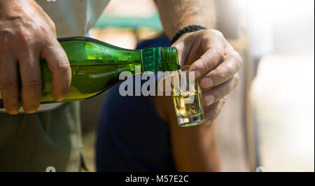 L'host versa brandy fatti in casa in una piccola bottiglia,mano versa un bicchiere di cognac dalla bottiglia. Foto Stock