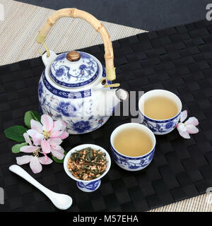 Giapponese fujiyama genmaicha tè con teiera orientali, foglie secche, tazze e la primavera sbocciano i fiori sul tappetino nero, bambù e ardesia sfondo. Foto Stock