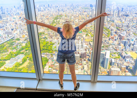 Vista aerea della skyline di Osaka in Giappone. Viaggi e turismo asia concetto. Giovani caucasici donna turistica con le braccia aperte godendo di Osaka cityscape dal ponte di osservazione. Foto Stock