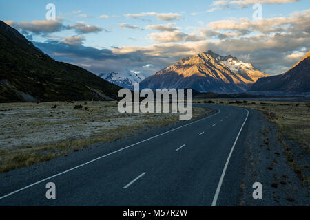 Una strada tortuosa attraverso Mt Cook Parco nazionale sull'Isola Sud della Nuova Zelanda. L'ultima luce del giorno si accende un picco ghiacciate in distanza Foto Stock