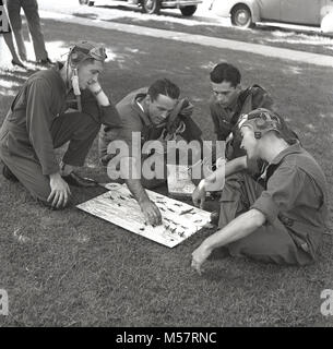 1942, STATI UNITI D'AMERICA, storico quattro soldati dell'esercito degli Stati Uniti le forze di aria (USAAF) indossare i loro battenti kit seduto su un orlo di erba fuori a giocare il nuovo gioco di bordo, 'combattimento aereo Trainer'. Prodotto in collaborazione con gli Stati Uniti reparto di guerra, il gioco era una prova di abilità di combattimento a battenti, utilizzando le miniature dei piani di guerra e manovre di combattimento. Foto Stock