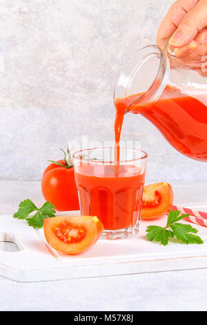 Versata a mano di succo di pomodoro da una brocca in vetro su un calcestruzzo di colore grigio nella tabella Foto Stock