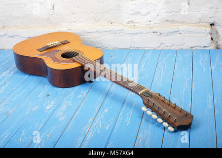 Strumento musicale - Vintage dodici-string chitarra acustica su un mattone di sfondo blu e pavimento in legno. Foto Stock