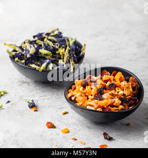 Frutta, erbe e tè di fiori in ciotole. La pietra grigia sullo sfondo Foto Stock