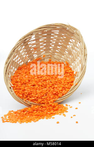Di lenticchie rosse sparse da un piccolo cesto isolato su bianco Foto Stock