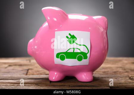 Primo piano di verde auto elettrica in rosa piggybank su legno Foto Stock