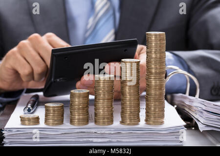 Sezione mediana di imprenditore calcolo fattura con monete impilate in ordine crescente a tavola Foto Stock