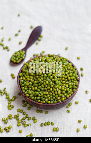 Mung bean, verde moong dal nella ciotola di legno. Bianco sfondo tessili. Vista dall'alto. Foto Stock