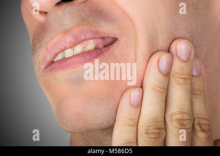 Closeup dell uomo che soffre di mal di denti contro uno sfondo grigio Foto Stock
