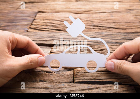 Immagine ritagliata di imprenditore il mano che tiene la carta auto elettriche al tavolo di legno Foto Stock