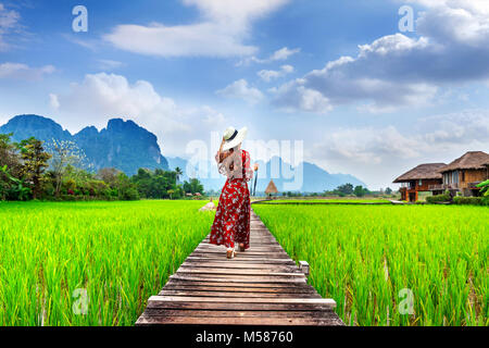 Giovane donna camminando sul percorso di legno verde con campo di riso in Vang Vieng, Laos. Foto Stock