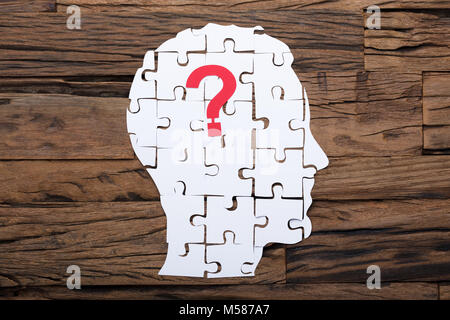 Imprenditore il capo costituito da carta puzzle pezzi e punto interrogativo sul tavolo di legno Foto Stock