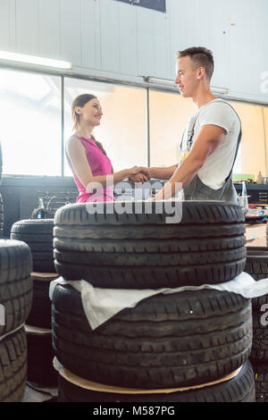 Bello meccanico automatico aiutando una femmina di cliente di scegliere tra vari di alta qualità di pneumatici in un contemporaneo automobile repair shop Foto Stock