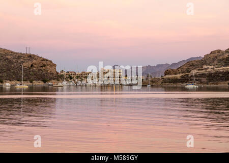 Bella rosa crepuscolo oscurata sky si riflette nelle calme acque di San Carlos bay con San Carlos Marina barche hotel negozi a distanza attraverso la baia di incandescente Foto Stock