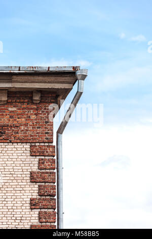 Angolo della vecchia casa di mattoni con tubo di drenaggio sul cielo blu sullo sfondo Foto Stock