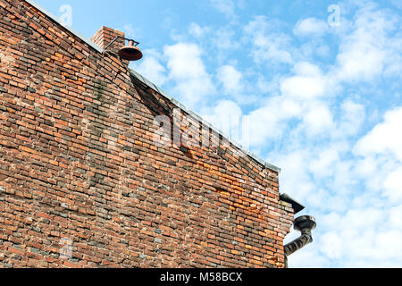 Casa un muro di mattoni a timpano con weathered drainpipe su un angolo e lanterna sul camino contro blu cielo molto nuvoloso Foto Stock
