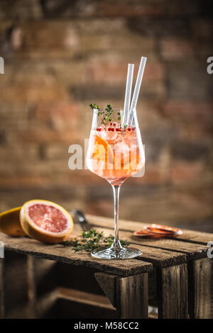 Cocktail di benvenuto su una vecchia tavola di legno. Bevanda alcolica con frutti tropicali pepe rosso di erbe e di ghiaccio. Foto Stock
