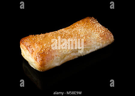 Rotolo di pasta sfoglia con semi di sesamo su sfondo nero Foto Stock