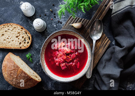 Ucraino zuppa Borscht servita con aneto fresco, pane e aglio su sfondo scuro. Cucina tradizionale Foto Stock