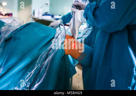 La chirurgia del ginocchio, ortopedico funzionamento - due chirurghi di eseguire un intervento chirurgico al ginocchio su un paziente (SHALLOW DOF; dai toni di colore immagine) Foto Stock