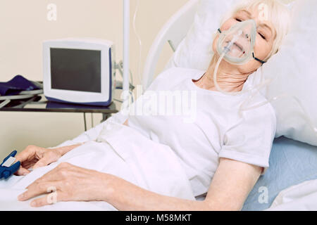 Senior donna con maschera di ossigeno e il pulsossimetro all'ospedale Foto Stock