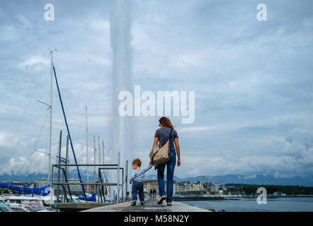 Una ragazza con un bambino sta tenendo le mani sul molo e lo sfondo di una grande fontana di Ginevra. Foto Stock