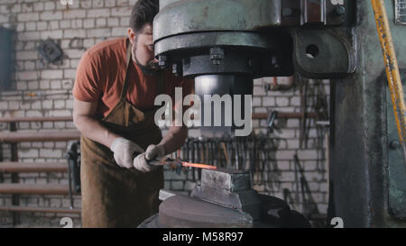 L'uomo fabbro in officina di un rosso di forgiatura ferro caldo sull'incudine - small business Foto Stock