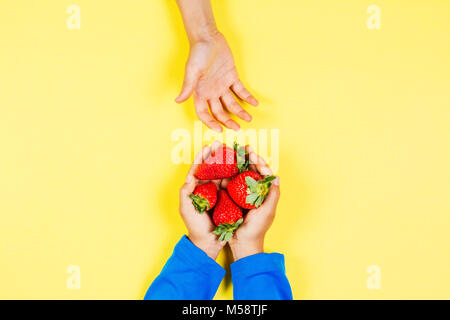 Kid mano tenendo fragola da un altro bambino con le mani in mano Foto Stock