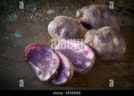 Fette di patate vitelotte, tre fette e tre patate intere su terreni accidentati sfondo scuro Foto Stock