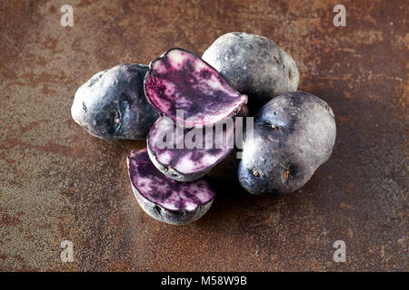 Fette di patate vitelotte, tre fette e tre patate intere su terreni accidentati sfondo scuro Foto Stock
