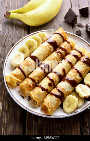 Gustosa crêpe rotolo con fette di banana sul tavolo di legno. Frittelle sottili, crepes con salsa di cioccolato. Vista superiore Foto Stock