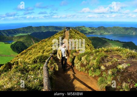 Viaggiatore a piedi in un percorso sterrato in tha cima di una montagna con una vista su una laguna volcaninc, montagne, oceano e cielo. Foto Stock