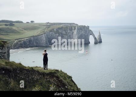 Donna in piedi su una collina di fronte Etretat famoso chalk cliff, arco e l'ago Foto Stock