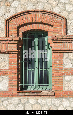 Finestra di un industriale del XIX secolo con la costruzione di un recinto verde su un impasto di cemento e un muro di mattoni. Foto Stock